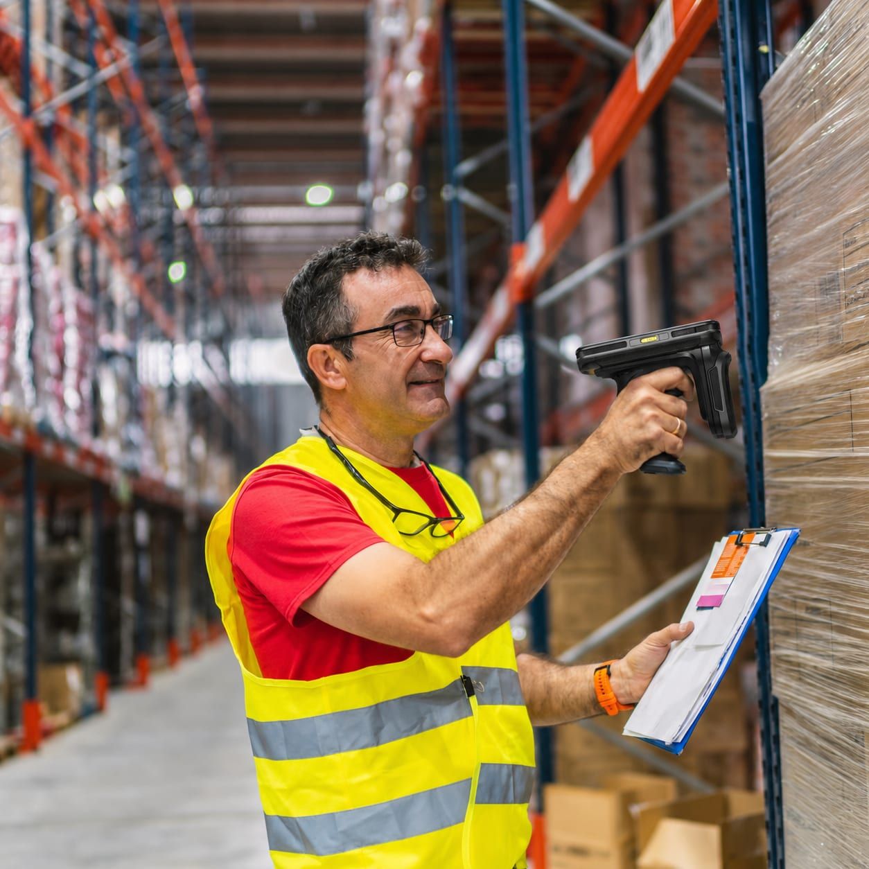 Een medewerker scant met een handscanner een etiket op een gewikkelde pallet dozen, met een klembord in de andere hand.