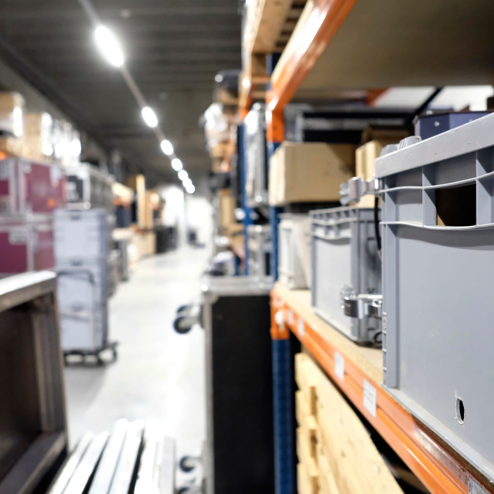 Gangpad in een verhuurmagazijn, met flightcases aan de ene kant en grijze stapelbakken in de stelling aan de andere kant.